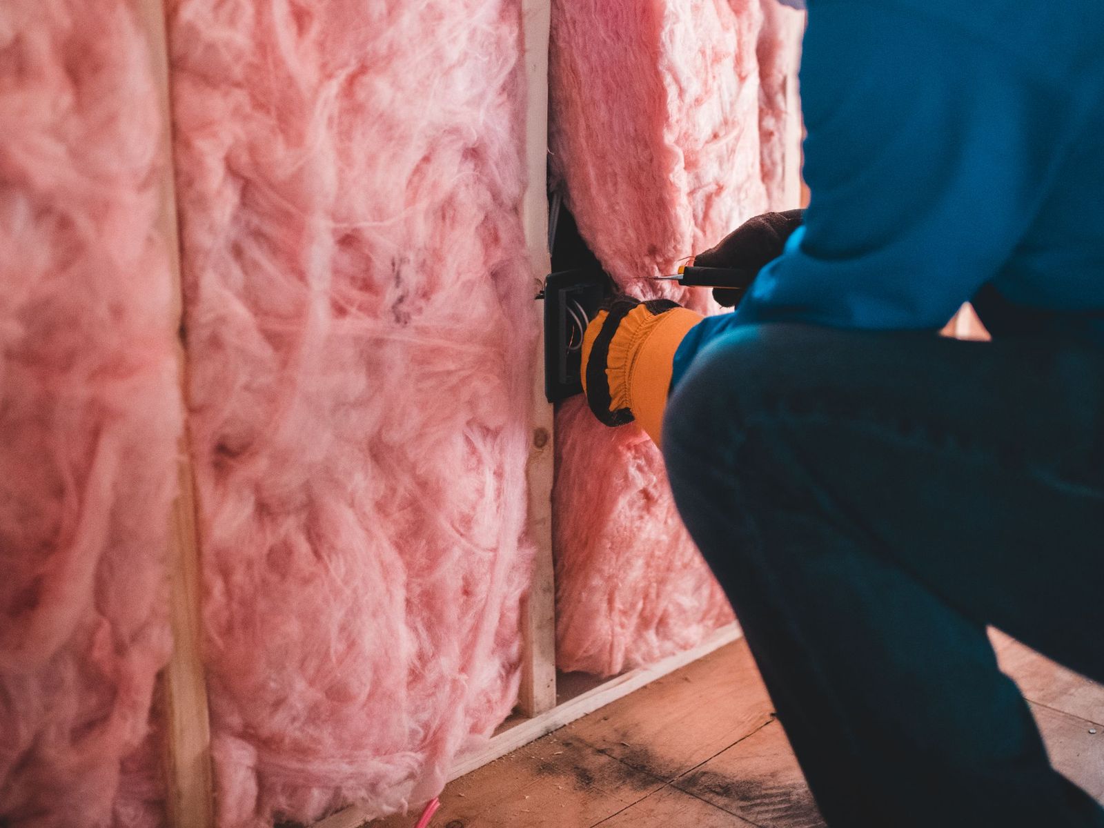 Gloved hands fitting fiberglass insulation between wall studs