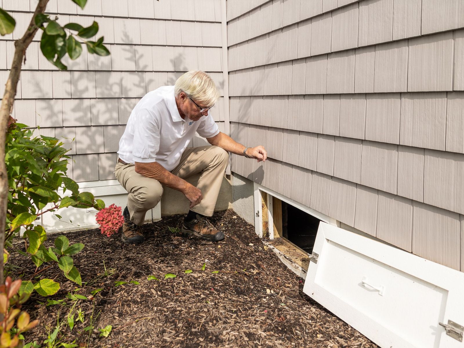 Opening the crawl space access panel on the side of a house